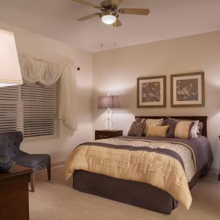 A cozy and well-decorated bedroom with neutral tones, featuring a comfortable bed, stylish lamps, framed artwork, and a plush chair.