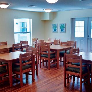 An empty dining area with wooden tables and chairs, featuring bright lighting and windows.