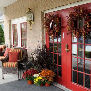 A welcoming front porch adorned with autumn wreaths, potted plants, and comfortable seating.