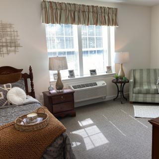 A cozy bedroom featuring a bed, armchair, and window with ample natural light.