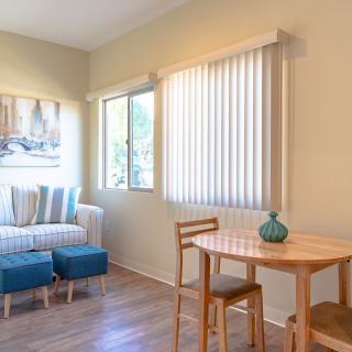 A cozy living room with a small table and chairs by the window, featuring a striped sofa and blinds.