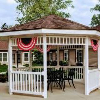A decorated gazebo with outdoor furniture surrounded by trees and a building.