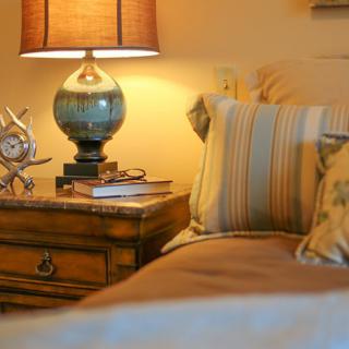 A cozy bedroom scene featuring a wooden nightstand adorned with a stylish lamp and decorative items, alongside a bed with striped pillows.