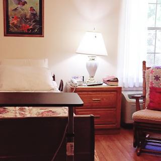 A cozy bedroom with a bed, nightstand, lamp, and a chair by the window.