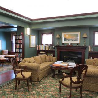 A cozy library room with comfortable seating, bookshelves, and a fireplace.