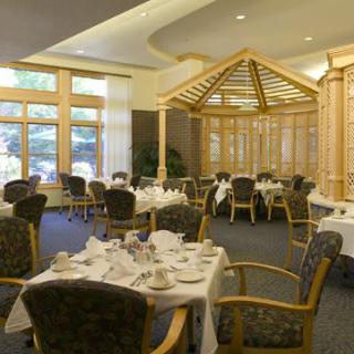 An elegant dining room setup with tables and chairs, bathed in natural light from large windows.