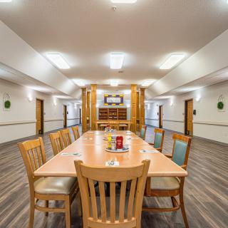A well-lit dining or meeting room with a long wooden table and chairs.