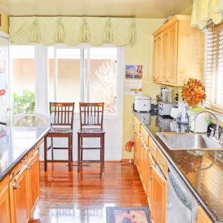 A bright kitchen featuring wooden cabinets, granite countertops, and two high chairs by the window.