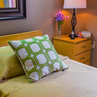 A cozy bedroom scene featuring a decorative pillow, a bedside lamp, and fresh flowers.