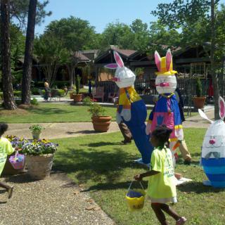 Children participate in an Easter egg hunt outside, surrounded by colorful bunny decorations.