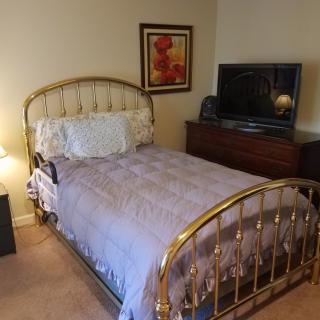 A cozy bedroom with a brass bedframe, television, and warm decor.