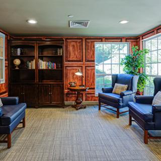 A cozy living room with blue chairs, a wooden bookshelf, and a warm atmosphere.