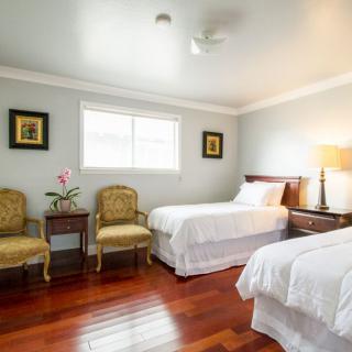 A cozy bedroom with two single beds, wooden floors, and ample natural light.