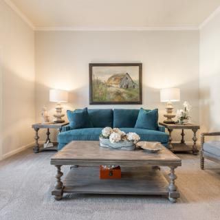A cozy living room with a teal sofa, wooden coffee table, elegant artwork, and decorative lamps.