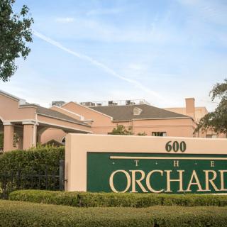 A residential complex with a sign labeled 'The Orchard' and surrounding greenery.