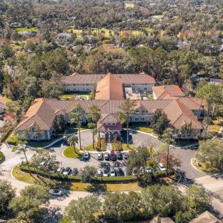 Aerial view of a sprawling residential building surrounded by lush greenery in a suburban setting.