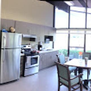 A modern kitchen featuring stainless steel appliances, a dining table, and large windows for natural light.