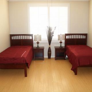 A neatly arranged bedroom with two twin beds, each with red bedding, alongside nightstands and lamps, facing a large window.