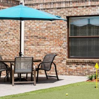 A cozy outdoor patio setup with a table, chairs, and an umbrella next to a golf putting green.