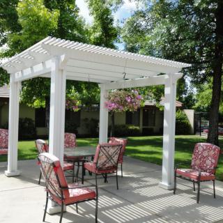 A beautiful outdoor patio area featuring a white pergola with hanging plants and comfortable seating.