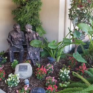 A serene garden scene featuring two statues seated among vibrant flowers and lush greenery.