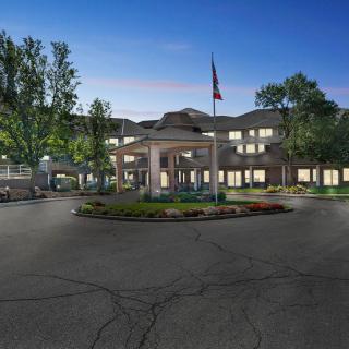 An elegant building with a circular driveway, surrounded by trees and lit up in the evening.
