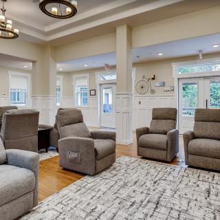 A modern living room featuring reclining chairs, a large rug, and natural lighting from multiple windows.