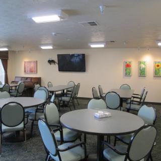 A well-lit dining area with round tables, chairs, a television, and artwork on the walls.