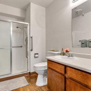 A modern, well-lit bathroom featuring a shower, toilet, and sink with wooden cabinets.