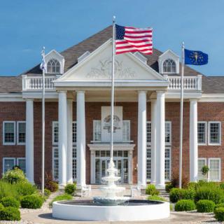 A majestic building with columns and a fountain, adorned with American and state flags.