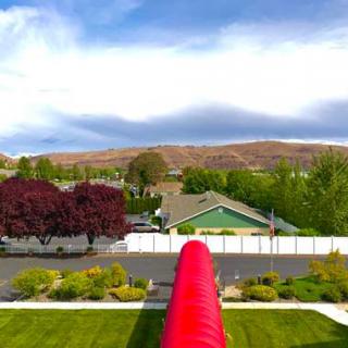 A scenic view of a neighborhood with lush greenery, houses, and a visible red slide under a partly cloudy sky.