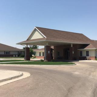 A building with an entrance featuring an awning and a circular driveway on a sunny day.