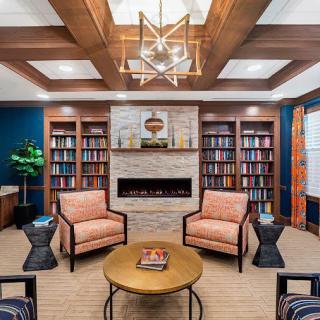 A cozy library room with a modern design featuring bookshelves, armchairs, and a fireplace.
