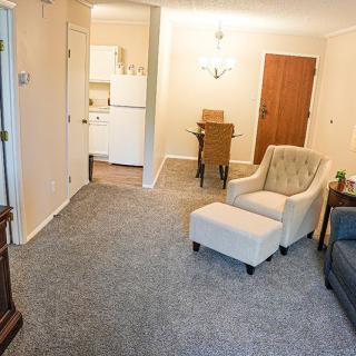 A cozy living room with an armchair, carpeted floor, and a view of the dining area.
