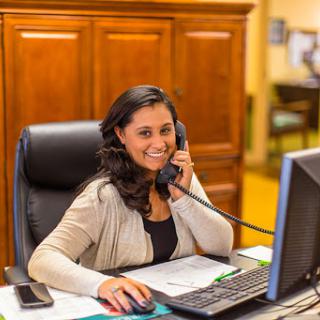 A cheerful woman working in an office, engaged in a phone call while sitting at her desk.