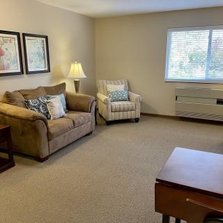 A cozy living room with a sofa, armchair, and a warm lamp by the window.