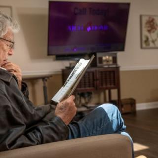 An elderly man is reading on a tablet while seated in a cozy living room.