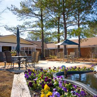 A serene outdoor space featuring a beautifully landscaped garden with vibrant flowers, comfortable seating, and sunlight filtering through the trees.
