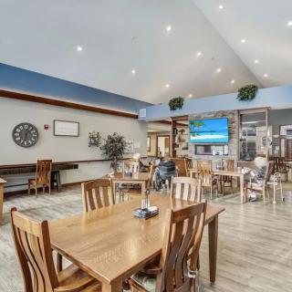 A modern dining area with wooden tables and chairs, featuring a television and decorative wall art.