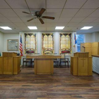 A courtroom interior featuring wooden furniture, flags, and a wooden floor.