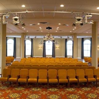 An empty conference room with rows of yellow chairs and projectors, ready for an event.