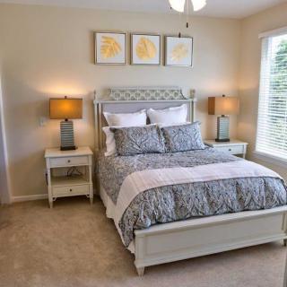 A modern bedroom with a neatly made bed, flanked by nightstands and lamps, decorated with artwork above the headboard.