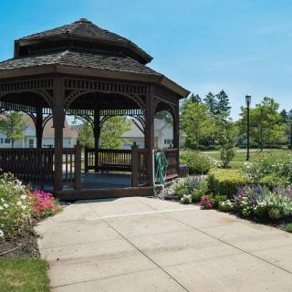 A charming gazebo surrounded by a well-maintained garden with colorful flowers and lush greenery on a sunny day.