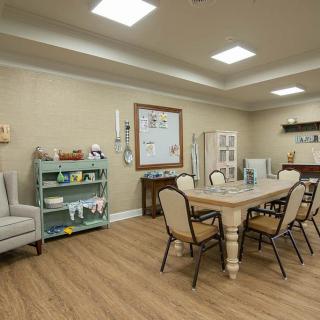 A cozy dining room with a large table, surrounded by chairs, and decorated with shelves and artwork.