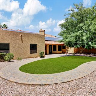 A beautifully landscaped residential home featuring a spacious lawn and patio area, under a clear blue sky.