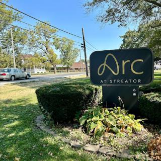The Arc sign located in a landscaped area, surrounded by trees and greenery.