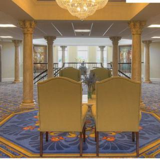 A spacious lobby with elegant chairs, ornate columns, and a decorative chandelier.