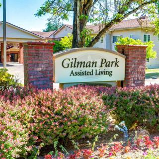 Entrance sign for Gilman Park Assisted Living surrounded by greenery.
