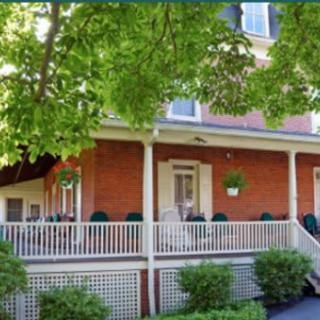 A charming brick house with a spacious porch surrounded by lush green trees.