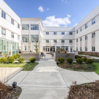 A modern building with a central courtyard and landscaped pathways under a partly cloudy sky.